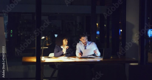 A business man and woman working overtime together to complete a project before the deadline. Young corporate people in the office late at night or evening completing paperwork on a nightshift photo
