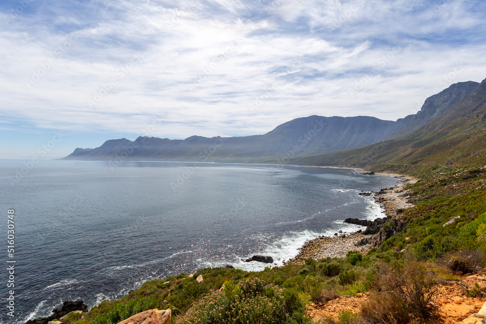 A breathtaking beach scene of majestic mountains, crystal-clear waters, and wispy clouds over a rugged coast. No People