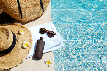 Swimming pool essentials concept. Beach bag with items for safe sunbathing on the deck, sunglasses, straw hat, white blanket & sunscreen product. Flat lay, copy space, top view, background.