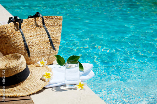 Swimming pool essentials concept. Beach bag with items for safe sunbathing on the deck, sunglasses, straw hat, white blanket & sunscreen product. Flat lay, copy space, top view, background.