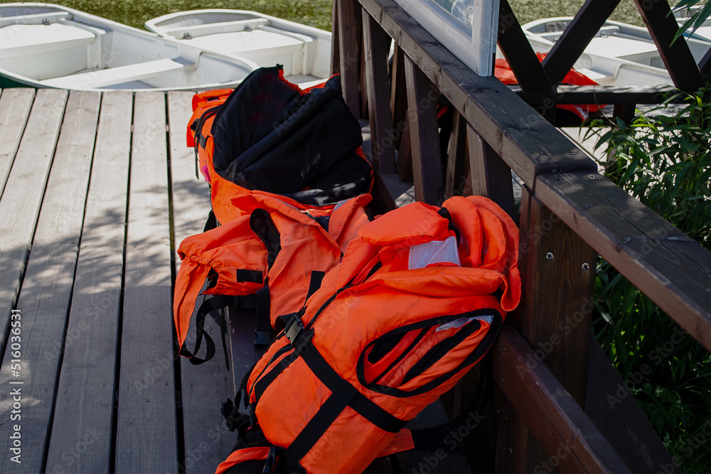 Fototapeta premium Bright orange life jackets lie on a bench at the boat station. Means of protection, rescue, safety.