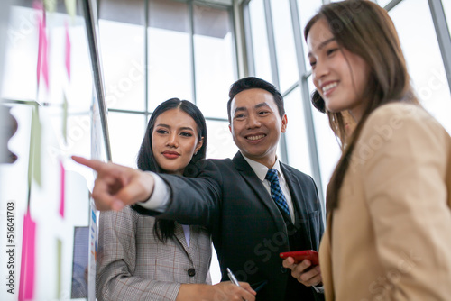 Asian business team male and female colleagues talking at work share ideas with chart on board, Happy young presenttation colleagues work together on board.