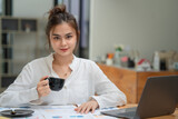 Businesswoman working with documents and drinking coffee in front of laptop computer at desk