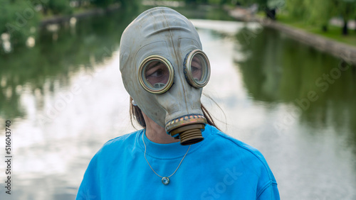 A girl in a gas mask stands on a bridge across the river. Alienation in the city. Fashion, ecology and loneliness concepts.