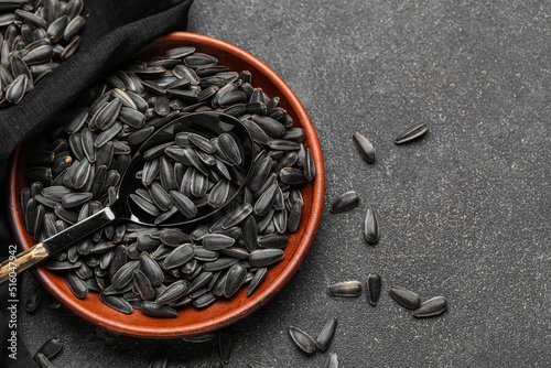 Bowl, spoon and napkin with black sunflower seeds on dark background