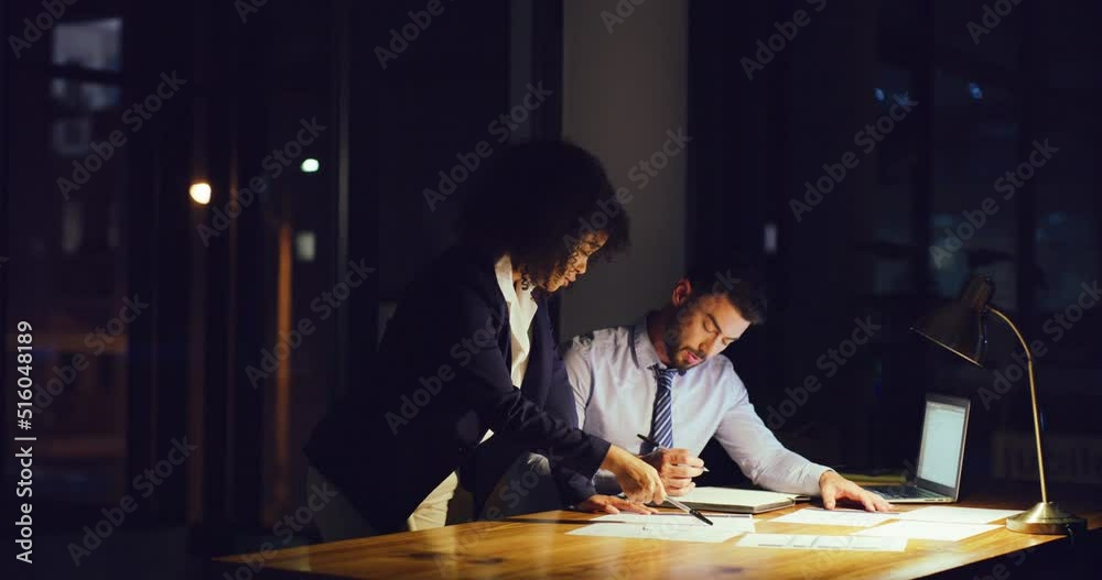 Two businesspeople having a discussion while working late in an office. Female leader or mentor giving instructions or ideas on paperwork with colleague at night. Accountants trying to reach deadline