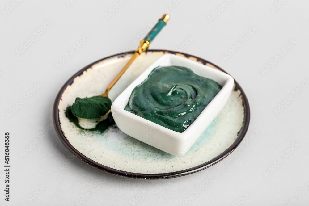 Plate with bowl of spirulina facial mask and powder on light background Plate with bowl of spirulina facial mask and powder on light background