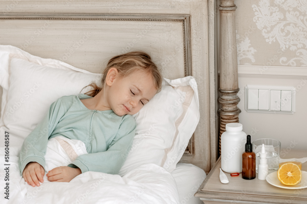 Sick child girl sleeping in bed at home. Cold flu treatment concept with lemon and medicine products. Copy space mock bottles pill Sick child girl sleeping in bed at home. Cold flu treatment concept with lemon and medicine products. Copy space mock bottles pill