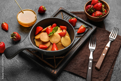 Composition with frying pan of mini pancakes and strawberry on dark background