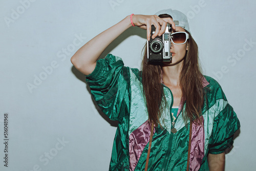 Cool teenager. Fashionable girl in colorful trendy jacket and vintage retro sunglasses with camera film in 80s - 90s style. Teenage girl at the disco, on a white background.