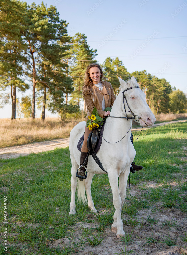  young beautiful smiling woman riding a white horse with blue eyes in autumn field  