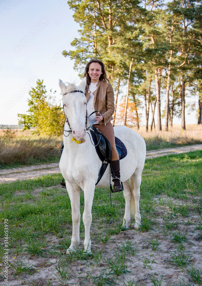  young beautiful smiling woman riding a white horse with blue eyes in autumn field  
