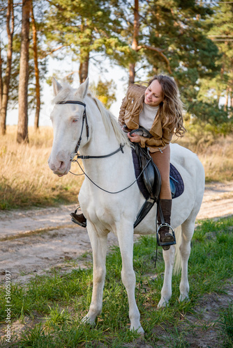  young beautiful smiling woman riding a white horse with blue eyes in autumn field 