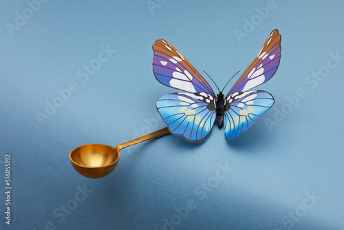 Blue butterfly siting on golden spoon and kipping balance on blue background. photo