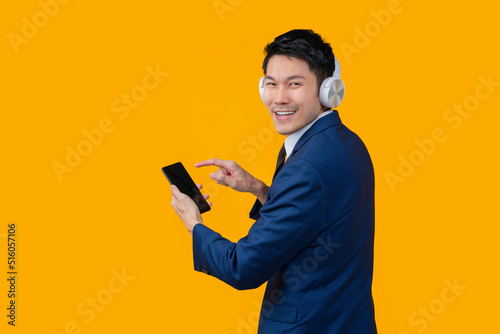 smart casual asian male business formal suit wear headphone while hand choosing playlist song from smartphone mobile application relax leisure after work isolate studio shot on yellow background