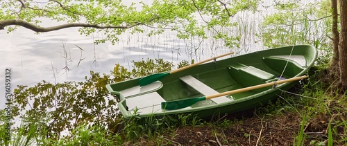 Small green boat anchored in forest lake. Scandinavia. Transportation, traditional craft, recreation, leisure activity, healthy lifestyle, local tourism, sport, rowing, hiking, summer vacations themes photo