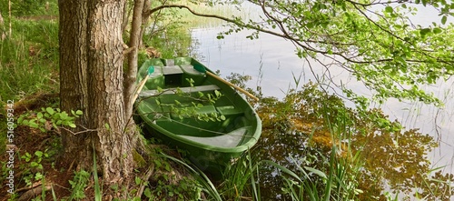 Small green boat anchored in forest lake. Scandinavia. Transportation, traditional craft, recreation, leisure activity, healthy lifestyle, local tourism, sport, rowing, hiking, summer vacations themes photo