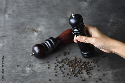 Hand holding pepperbox mill isolated on dark wood background. photo