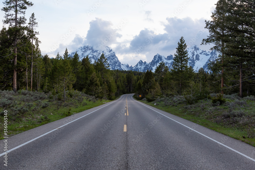 Scenic Road surrounded by Mountains and Trees in American Landscape. Spring Season. Grand Teton National Park. Wyoming, United States. Nature Background. Scenic Road surrounded by Mountains and Trees in American Landscape. Spring Season. Grand Teton National Park. Wyoming, United States. Nature Background.