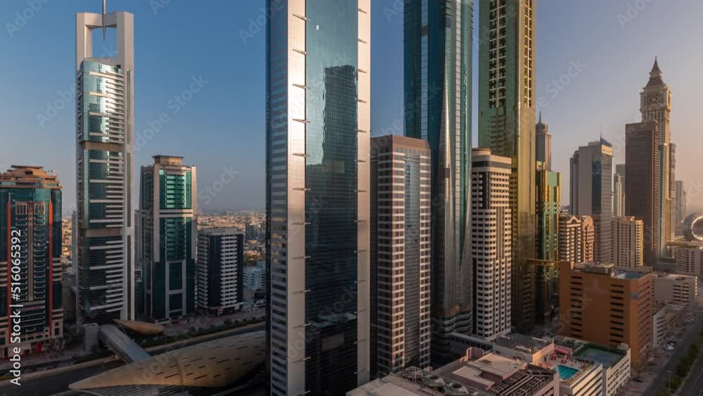 Aerial view of Dubai International Financial District with sun reflected from skyscrapers during sunrise timelapse. Traffic on a road near multi storey parking with rooftop swimming pool. Dubai, UAE.