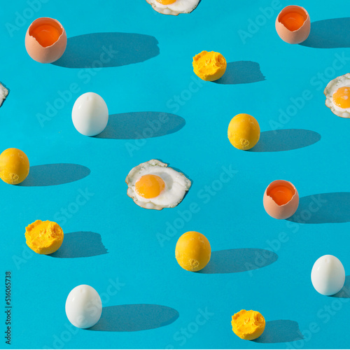 Colorful pattern made of raw cracked egg, boild eggwhite, yolk and sunny side up egg on blue background with long shadow. Square composition with copy space.