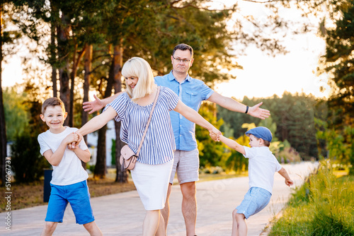 Two naughty boys pulls their mother by the hands, wanting to stay at park. The capricious children resists and does not want to leave. Upset confused father spreading his arms stand behind