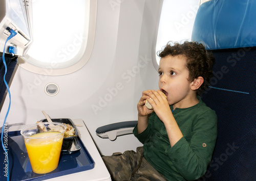 child in airplane seat eating while looking at the screen