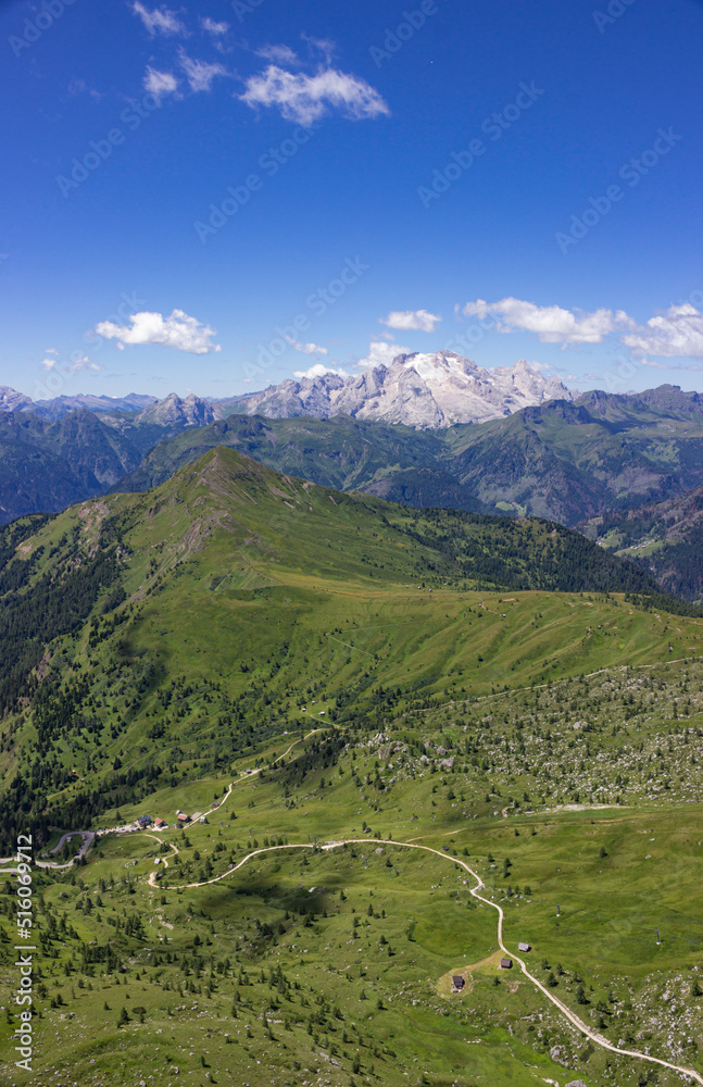 Mountain summer landscape. Grassy meadows and rocks under the blue sky. Marmolada glacier, Italy. High quality vertical image.