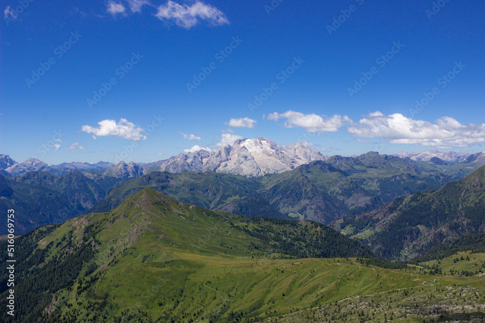Mountain summer landscape. Grassy meadows and rocks under the blue sky. Marmolada glacier, Italy. Climate change concept. High quality image.