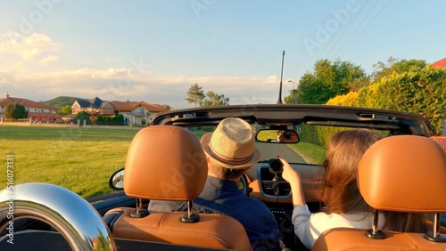 Couple in cabriolet car driving, arriving home in late sunlight.