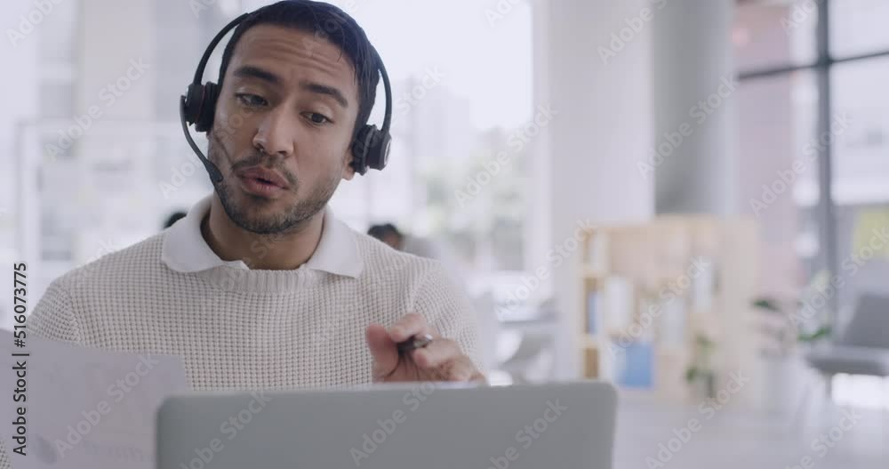 Confident businessman using a laptop and headset on a conference call in a modern office. Young professional man discussing business plan with investors. Rep or customer service agent calling client