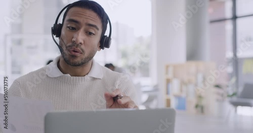 Confident businessman using a laptop and headset on a conference call in a modern office. Young professional man discussing business plan with investors. Rep or customer service agent calling client