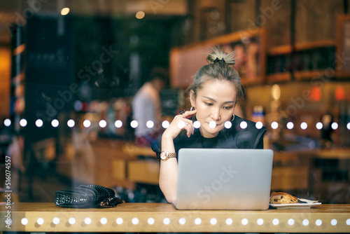 asian business woman sitting by the window in coffee shop working using laptop computer photo