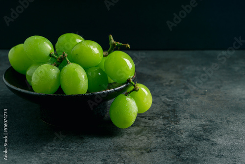 A branch of green juicy grapes in a plate with copy space. Black background. Front view. Place for writing. Suitable for Summer.