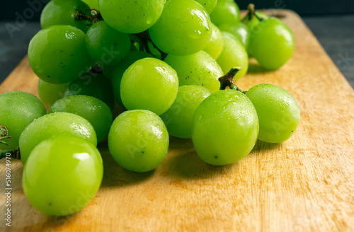 Fresh Green grapes on a wooden cutting board. Shooting in the dark. Close up view. Bunch of grapes on a wooden grey background. Space for writing. Suitable for summer.