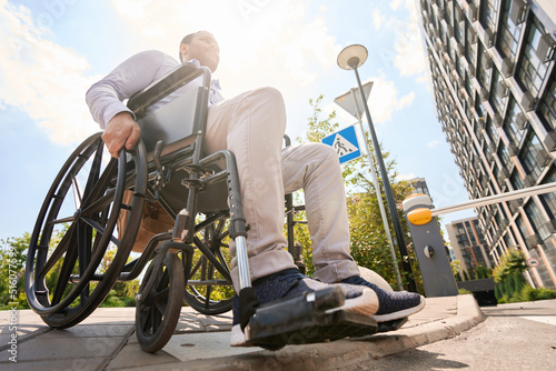 Foto Wheelchair-bound young man is descending sidewalk curb