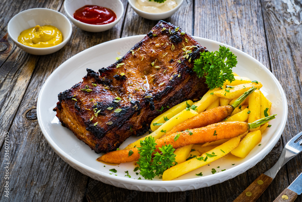 Tasty grilled ribs with french fries and caramelized carrots on wooden table Tasty grilled ribs with french fries and caramelized carrots on wooden table