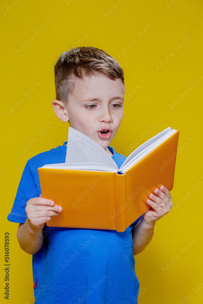 Positive preschool boy in an blueT-shirt holding an open yellow copybook on yellow background Positive preschool boy in an blueT-shirt holding an open yellow copybook on yellow background