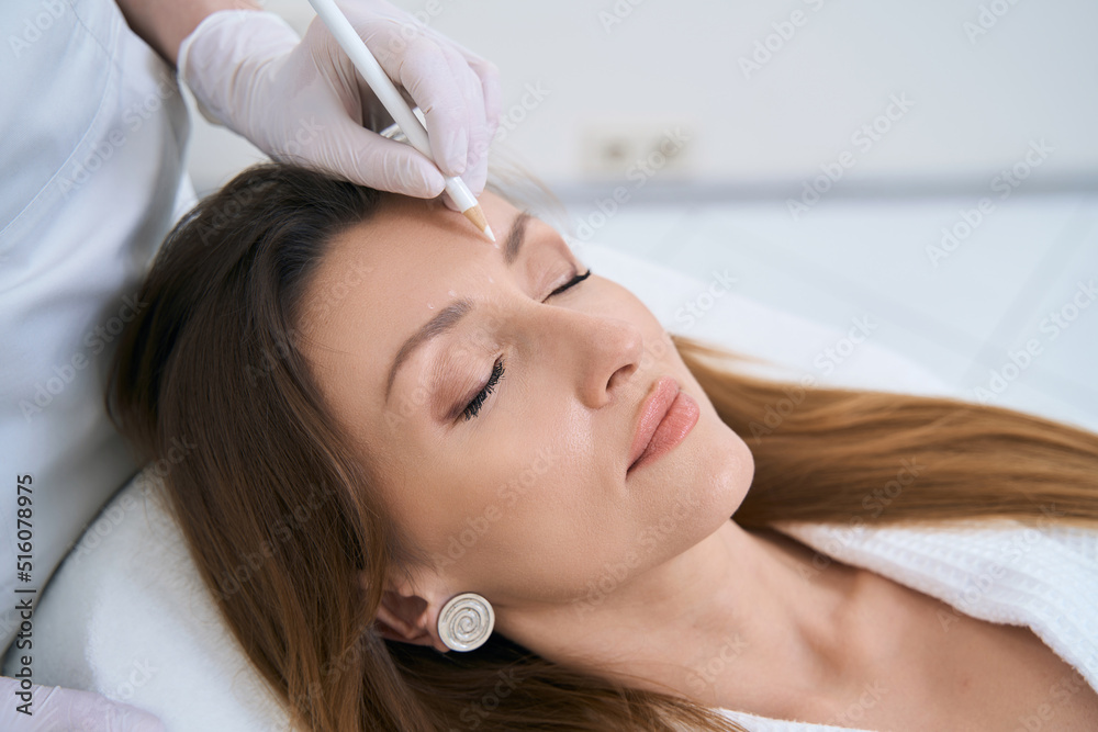 Naklejka premium Beautician marks patient skin on forehead for injection