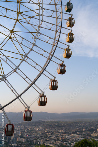 Famous ferris wheel in Mtatsminda amusement park in Tbilisi, Georgia. Giant wheel with cabins at sunset, city and mountain on background. Entertainment concept
