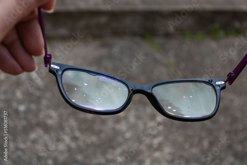 Close up of dirty eye glasses with water drops held by a female hand