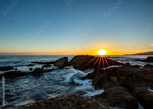 Sun Setting over a rock in Laguna Beach California.  Waves Crashing.