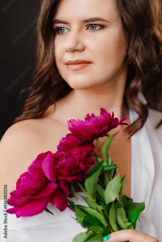 A peaceful brunette woman in white clothes with a bouquet of peonies.