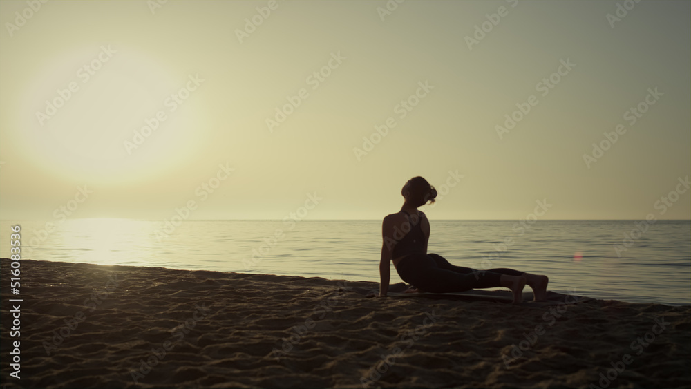 Silhouette sportswoman making plank pose practicing yoga. Girl training on beach