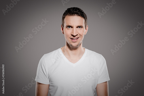 stupid and mindless face expression of man while look at camera and show his questioning  emotions with eyes and glimpse at camera isolated on gray background photo