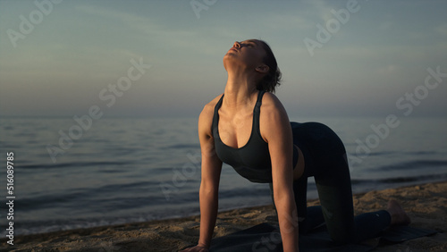 Sportswoman making cat cow pose practicing yoga on sandy beach close up. 