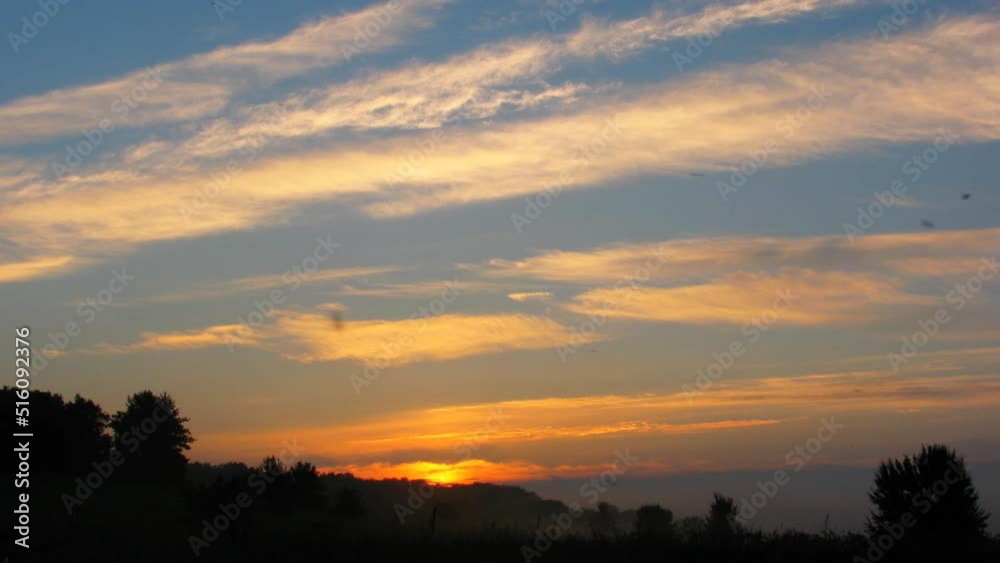 Dawn and sunrise over a meadow in the countryside. Summer morning. Light clouds and fog. Orange clouds in the blue sky. Timelapse Dawn and sunrise over a meadow in the countryside. Summer morning. Light clouds and fog. Orange clouds in the blue sky. Timelapse