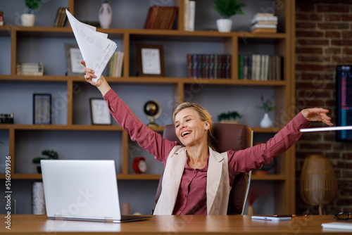 Female worker celebrating the successful end of working day at office. Happy businesswoman throwing up papers with graphs and charts. Calm manager with falling papers around dreaming about vacation