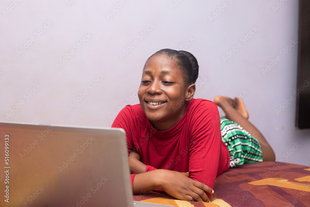 A young black teenage girl smiling looking laptop whilst lying on bed A young black teenage girl smiling looking laptop whilst lying on bed