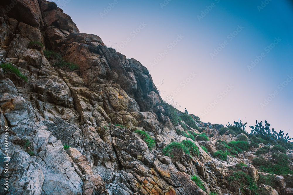 Rocky terrain with steep rough cliffs and scattered weeds. Mountain limestone rocks texture